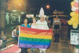 Manifestantes segurando a bandeira. Militante fantasiado de papa insentiva o uso de preservativo.